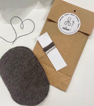 Reparationskit med brun papperspåse märkt med "Repair – Reuse – Reduce", svart tråd formad som ett hjärta, garnprov och en bit mörkgrå ull på vit bakgrund.